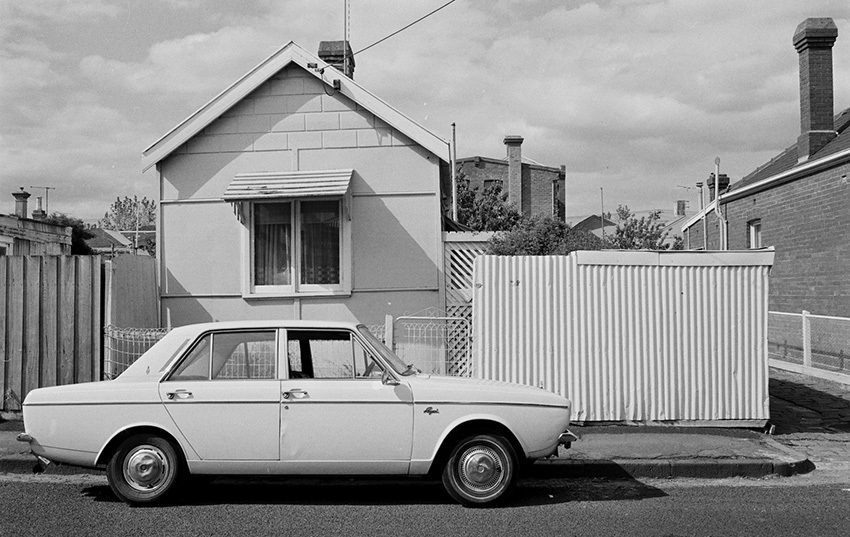 Chalk inscription on roadway, three storey block of flats on the north-east corner of Erskine and Harold Streets, single storey brick house with gabled roof, single storey wooden house with veranda, corrugated iron garage, small house with gabled roof and corrugated iron fence fronting the yard, Federation style brick house, brick house with gabled roof, side-front view of the two story terraced house on the north-west corner of Erskine and Nimmo Streets, Middle Park.